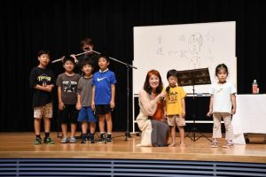 記念講演の中で子供たちと共に「チューリップ」を歌ういらみなさん（右から３人目）＝８日、市未来創造センター