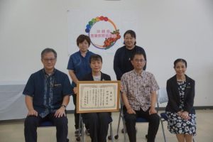 崎間副会長（前列右から２人目）から産業教育功労者表彰を伝達された砂川さん（同３人目）ら＝17日、県教育庁