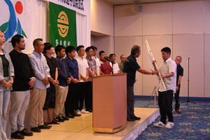 結団式で砂川団長（右から３人目）が石原さん（同２人目）に団旗を授与した＝７日、ホテルアトールエメラルド宮古島