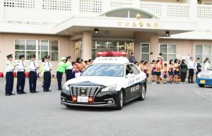 出発式でパトカーを見守る署員と防犯協会、ボランティアの皆さん＝16日、宮古島署