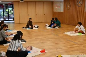新里さん（右奥）の指導を受けてマッサージを行った母親たち＝1月31日、はなぞのこどもえん