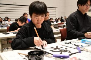 真剣な表情で筆を走らせる参加者ら＝11日、市未来創造センター多目的ホール