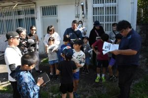 久貝さん（手前右）の説明に聞き入る参加者たち＝18日、保良村総代平良真牛生誕地之碑