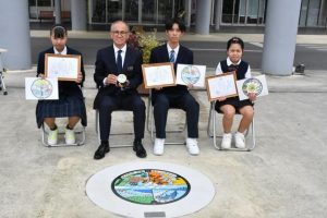 マンホールふたデザインの入賞者ら。(左から)砂川さん、嘉数市長、竹野さん、荷川取さん=22日、市役所正面玄関前