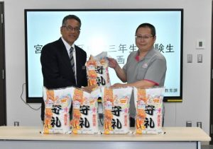 合格応援米の「愛を米無洗米　守礼５㌔」を手渡す佐久田さん（右）＝４日、市役所