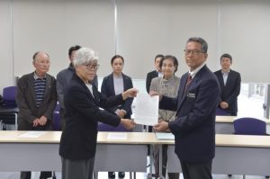 メンバーが見守る中、新崎代表（手前左）から宮城教育長に要請書が手渡された＝12日、市役所