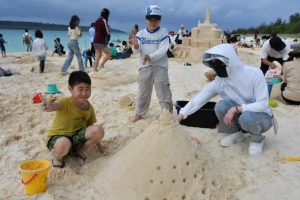 砂遊びを楽しむ親子連れ。右後方に見える城が佐田さんの作品＝22日、前浜ビーチ