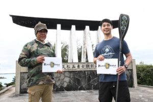 「ＫＵＲＩＭＡ　ＴＡＲＡＭＡ」挑戦する来間さん（右）。船で伴走する奥平さん＝９日、久松五勇士顕彰碑前