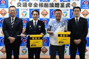 横断旗を寄贈した阪口支店長（左）、宮下淳一沖縄支店地域戦略室長（右）と受け取った新垣署長（中央左）、石原副会長（中央右）＝19日、宮古島署