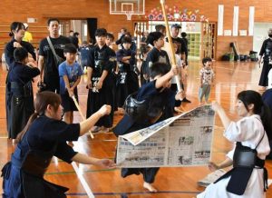 佐藤さん（右）の指導を受け、新聞紙切りに挑戦する少年剣士＝21日、北小体育館